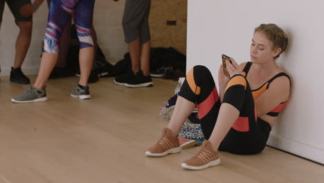 beautiful-caucasian-woman-dancer-using-smartphone-in-dance-studio-texting-sharing-practice-on-social-media-resting-after-intense-workout-exercise