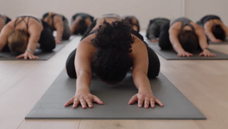 yoga-class-instructor-teaching-group-of-young-women-childs-pose-on-exercise-mat-enjoying-healthy-lifestyle-training-meditation-practice-in-fitness-studio