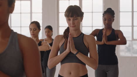 beautiful-caucasian-yoga-woman-practicing-warrior-pose-meditation-with-group-of-multiracial-women-enjoying-healthy-lifestyle-exercising-in-fitness-studio-at-sunrise