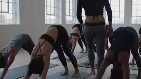 yoga-class-instructor-teaching-downward-facing-dog-pose-group-of-women-practicing-enjoying-healthy-lifestyle-exercising-in-fitness-studio-at-sunrise