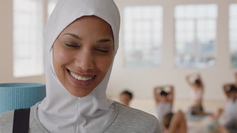 Porträt-Einer-Schönen-Muslimischen-Yoga-Frau,-Die-Selbstbewusst-Lächelt-Und-Einen-Gesunden-Lebensstil-Mit-Hijab-Kopftuch-Genießt,-Während-Menschen-Im-Hintergrund-Im-Fitnessstudio-üben
