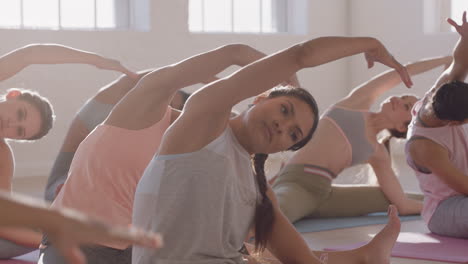 Yoga-Kurs:-Gesunde-Hispanische-Frau-übt-Sitzende-Seitenbeuge-Pose-Mit-Einer-Gruppe-Schöner-Frauen,-Die-Auf-Einer-Trainingsmatte-Sitzen-Und-Bei-Sonnenaufgang-Ein-Training-Für-Einen-Gesunden-Lebensstil-Im-Fitnessstudio-Genießen