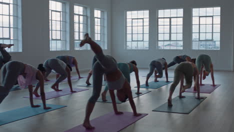 yoga-class-of-healthy-women-practicing-one-legged-downward-facing-dog-pose-enjoying-exercising-in-fitness-studio-instructor-leading-group-meditation-teaching-workout-posture-at-sunrise