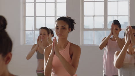 yoga-class-healthy-mixed-race-woman-practicing-prayer-pose-with-group-of-beautiful-women-enjoying-healthy-lifestyle-exercising-in-fitness-studio-training-at-sunrise