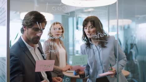 business-people-using-sticky-notes-young-team-leader-man-brainstorming-with-colleagues-writing-ideas-on-glass-whiteboard-working-on-solution-discussing-strategy-teamwork-in-office-meeting-4k