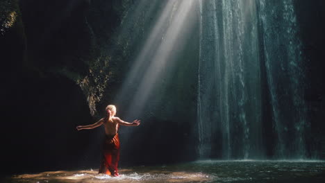 Tanzende-Frau-In-Der-Wasserfallhöhle,-Die-Wasser-Spritzt-Und-Ein-Wunderschönes-Kleid-Trägt,-Genießt-Die-Natur,-Tanzt-Und-Fühlt-Spirituelle-Freiheit-4k
