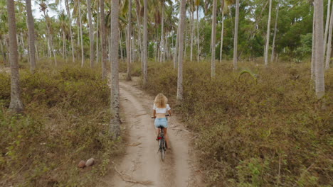 Vista-Aérea-Mujer-Montando-Bicicleta-Explorando-Isla-Tropical-Chica-Viajando-Disfrutando-Del-Hermoso-Bosque-De-Palmeras-4k