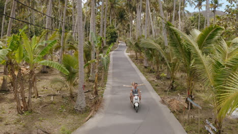 Vista-Superior-Pareja-Montando-Scooter-En-Una-Isla-Tropical-Explorando-El-Bosque-De-Palmeras-En-Motocicleta-Los-Turistas-Exploran-El-Destino-De-Vacaciones-Con-Moto
