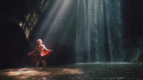 Mujer-Bailando-En-Una-Cueva-De-Cascada-Salpicando-Agua-Con-Un-Hermoso-Vestido-Disfrutando-De-La-Naturaleza-Bailando-Sintiendo-Libertad-Espiritual-4k