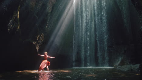 Tanzende-Frau-In-Der-Wasserfallhöhle,-Die-Wasser-Spritzt-Und-Ein-Wunderschönes-Kleid-Trägt,-Genießt-Die-Natur,-Tanzt-Und-Fühlt-Spirituelle-Freiheit-4k