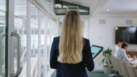 rear-view-blonde-business-woman-walking-through-office-holding-tablet-computer-enjoying-successful-leadership-career-in-corporate-workplace-4k