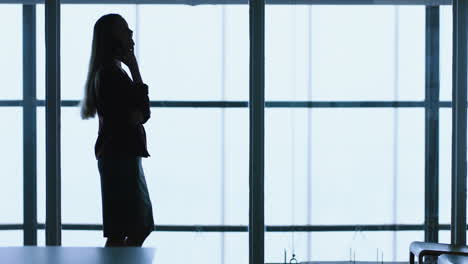 silhouette-business-woman-using-smartphone-having-phone-call-chatting-on-mobile-phone-talking-with-client-at-work-in-office-4k