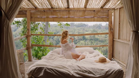 Eine-Reisende-Frau-Trinkt-Kaffee-Im-Bett-Eines-Tropischen-Hotelresorts-Und-Genießt-Einen-Entspannten-Morgen-Mit-Blick-Auf-Den-Dschungel