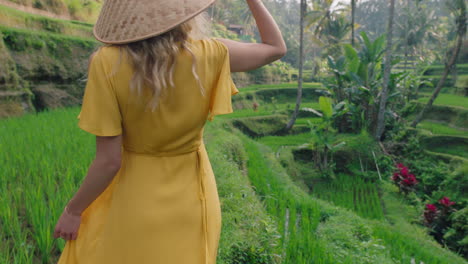 Mujer-Caminando-En-Un-Arrozal-Con-Un-Vestido-Amarillo-Con-Sombrero-Cónico-Explorando-Una-Exuberante-Terraza-De-Arroz-Verde-En-Un-Paisaje-Cultural-Vacaciones-Exóticas-A-Través-De-Bali-Indonesia-Descubre-Asia