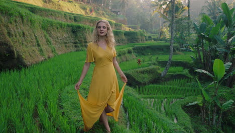 Hermosa-Mujer-Caminando-En-Un-Arrozal-Con-Un-Vestido-Amarillo-Explorando-Un-Exuberante-Campo-De-Arroz-Verde-Vacaciones-Exóticas-En-Bali,-Indonesia