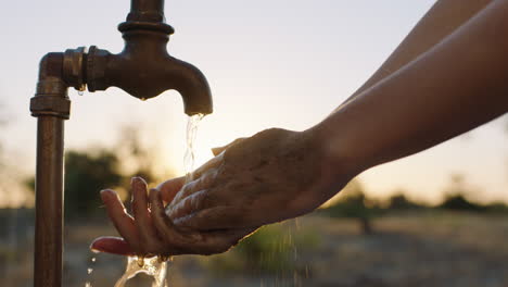 close-up-woman-washing-dirty-hands-under-tap-with-fresh-water-on-rural-farmland-at-sunset