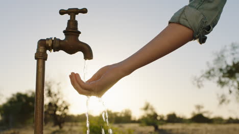woman-hands-catching-water-under-tap-thirsty-farmer-drinking-freshwater-flowing-from-faucet-at-sunset-save-water-concept