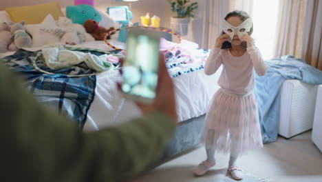 Fröhliches-Kleines-Mädchen,-Das-Im-Schlafzimmer-Mit-Maske-Spielt,-Während-Die-Mutter-Mit-Dem-Smartphone-Ein-Foto-Macht-Und-Es-In-Sozialen-Medien-Teilt
