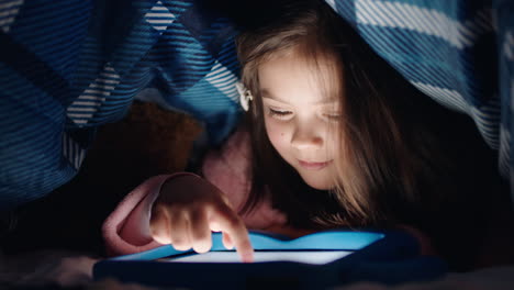 Fröhliches-Kleines-Mädchen,-Das-Unter-Einer-Decke-Einen-Digitalen-Tablet-Computer-Benutzt,-Das-Lernen-Auf-Touchscreen-Technologie-Genießt,-Spiele-Spielt-Und-Vor-Dem-Schlafengehen-Spaß-Hat