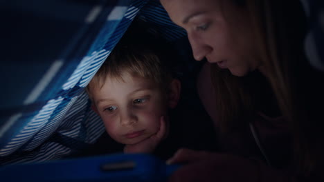 Glückliche-Mutter-Und-Sohn,-Die-Unter-Der-Decke-Einen-Tablet-Computer-Benutzen.-Kleiner-Junge-Spielt-Spiele-Auf-Touchscreen-Technologie,-Während-Sich-Die-Mutter-Vor-Dem-Schlafengehen-Entspannt-Und-Spaß-Hat