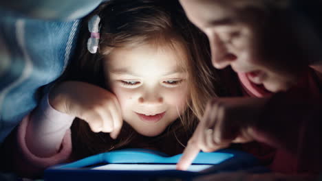 Glückliche-Mutter-Und-Tochter,-Die-Unter-Der-Decke-Einen-Tablet-Computer-Benutzen-Und-Spiele-Auf-Touchscreen-Technologie-Spielen,-Sich-Entspannen-Und-Vor-Dem-Schlafengehen-Spaß-Haben