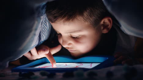 Fröhlicher-Kleiner-Junge,-Der-Unter-Einer-Decke-Einen-Digitalen-Tablet-Computer-Benutzt-Und-Spaß-Daran-Hat,-Auf-Der-Touchscreen-Technologie-Zu-Lernen,-Spiele-Zu-Spielen-Und-Vor-Dem-Schlafengehen-Spaß-Zu-Haben