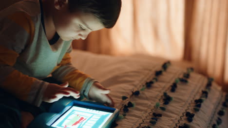 Fröhlicher-Kleiner-Junge,-Der-Einen-Digitalen-Tablet-Computer-Benutzt,-Der-Auf-Dem-Bett-Sitzt-Und-Das-Zeichnen-Genießt,-Auf-Der-Touchscreen-Technologie-Lernt,-Spiele-Spielt-Und-Vor-Dem-Schlafengehen-Spaß-Hat