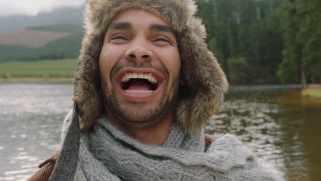 portrait-young-man-laughing-feeling-happy-wearing-fur-hat-outdoors-in-nature-by-lake
