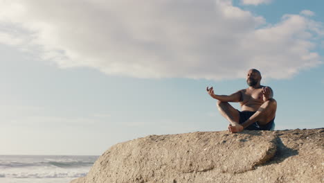 Afroamerikanischer-Mann-Meditiert-Am-Strand-Und-übt-Achtsamkeit,-Entspannt-Sich-Im-Freien-Und-Genießt-Die-Ruhige-Küste-In-4K