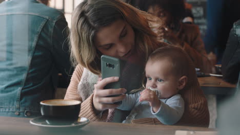 young-mother-with-baby-in-cafe-using-smartphone-drinking-coffee-relaxing-in-busy-restaurant-enjoying-motherhood