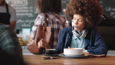Schöne-Frau-Mit-Afro,-Die-Ihr-Smartphone-Im-Café-Benutzt-Und-Kaffee-Trinkt,-SMS-Schreibt-Und-Nachrichten-In-Sozialen-Medien-Teilt-Und-Mobile-Technologie-In-Einem-Belebten-Restaurant-Genießt