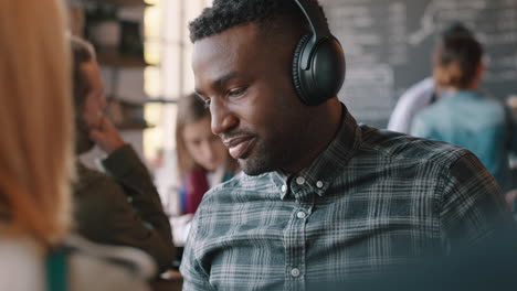 Junger-Afroamerikanischer-Mann-Benutzt-Smartphone-Im-Café,-Surft-Online-Und-Genießt-Unterhaltung,-Hört-Musik-Und-Trinkt-Kaffee-In-Einem-Belebten-Restaurant