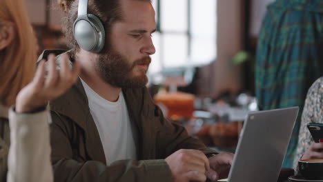 Junger-Mann-Benutzt-Laptop-Im-Café,-Surft-Online-Und-Hört-Musik,-Trägt-Kopfhörer-Und-Genießt-Mobile-Computertechnologie