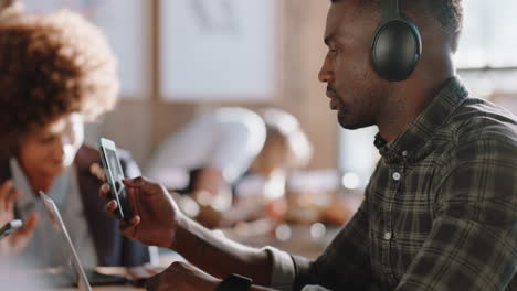 Junger-Afroamerikanischer-Mann-Benutzt-Laptop-Im-Café-Und-Surft-Online,-Checkt-Nachrichten-Auf-Dem-Smartphone-Und-Hört-Musik,-Während-Er-Im-Café-Arbeitet