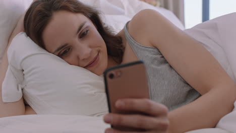 Schöne-Frau,-Die-Ihr-Smartphone-Im-Bett-Benutzt-Und-SMS-Schreibt,-Social-Media-Nachrichten-Teilt-Und-Eine-Online-Verbindung-Genießt-Und-Sich-Zu-Hause-Entspannt