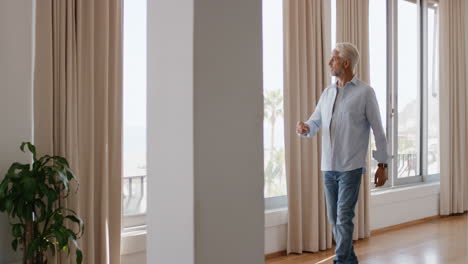 Reifer-Mann-Im-Hotelzimmer-Im-Urlaub,-Der-Aus-Dem-Fenster-Schaut,-über-Seinen-Lebensstil-Nachdenkt-Und-Einen-Entspannten-Ruhestand-Genießt