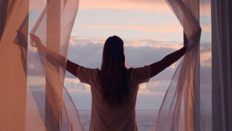 happy-woman-opening-curtain-enjoying-early-morning-sunrise-at-home-feeling-peaceful-freedom-relaxing-on-vacation-looking-at-beauiful-ocean-view