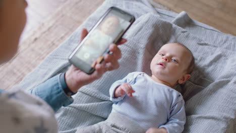 Madre-Feliz-Tomando-Una-Foto-De-Un-Bebé-Usando-Un-Teléfono-Inteligente-Disfrutando-Fotografiando-A-Un-Lindo-Niño-Pequeño-Compartiendo-Su-Estilo-De-Vida-Maternal-En-Las-Redes-Sociales