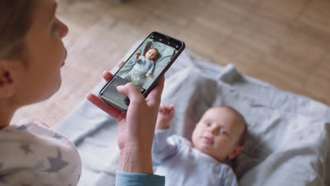 Madre-Feliz-Tomando-Una-Foto-De-Un-Bebé-Usando-Un-Teléfono-Inteligente-Disfrutando-Fotografiando-A-Un-Lindo-Niño-Pequeño-Compartiendo-Su-Estilo-De-Vida-Maternal-En-Las-Redes-Sociales