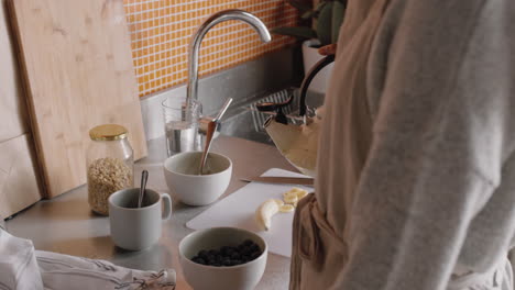 young-woman-in-kitchen-making-hot-coffee-boiling-kettle-pouring-water-into-cup-getting-ready-for-breakfast-at-home