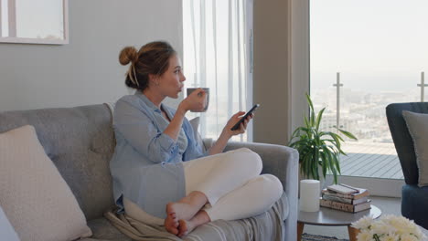 Schöne-Junge-Frau-Mit-Smartphone-Entspannt-Zu-Hause-Auf-Der-Couch,-Surft-Online-Und-Schreibt-SMS,-Trinkt-Kaffee-Und-Genießt-Einen-Komfortablen-Lebensstil