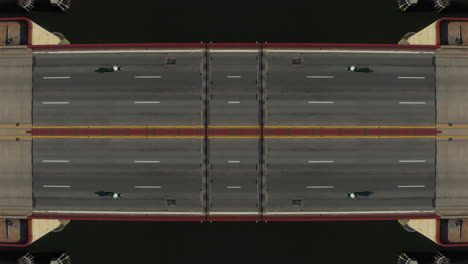 Top-down-ascending-footage-of-cars-passing-on-bridge-over-water,-symmetrical-composition.-Abstract-computer-effect-digital-composed-footage