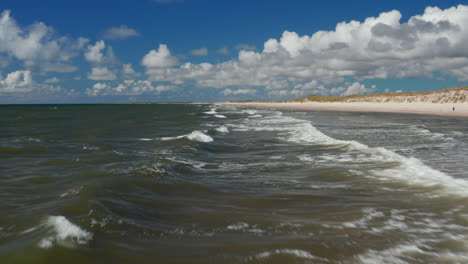 Waves-rolling-on-water-surface.-Low-flights-above-rippled-sea-near-coast.-Sand-beach-and-green-vegetation-on-shore.-Denmark