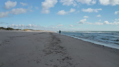 Forwards-tracking-of-person-running-on-beach.-Sands-in-cloud-shadow.-Waves-washing-sea-coast.-Denmark