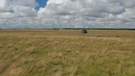 Drivers-giving-way-to-other-cars-and-cyclists-on-narrow-country-road-through-vast-flat-grasslands.-Denmark