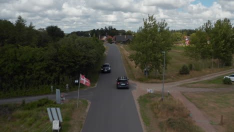 Forwards-tracking-of-car-passing-through-village.-Danish-flags-on-poles-along-street.-Horses-grazing-on-fresh-green-grass.-Denmark