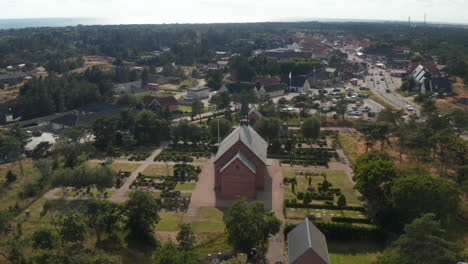 Aerial-footage-of-cemetery-around-wooden-church-or-chapel.-Buildings-in-small-town-in-background.-Flat-landscape-with-trees.-Denmark
