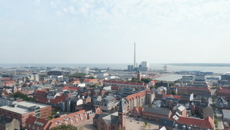 Forward-slow-flight-over-the-city-of-Esbjerg-with-the-Church-of-Our-Saviour.-Bird's-eyes-revealing-his-harbor-with-the-chimney-of-the-coal-and-oil-fueled-power-plant,-the-tallest-in-Scandinavia