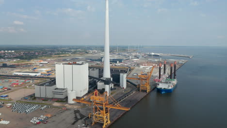 Slow-rotation-birds-eye-over-the-Esbjerg-harbor-and-the-chimney-of-the-Steelcon-coal-fired-power-station.-Aerial-view-revealing-the-harbor-in-the-background,-the-most-important-of-the-north-sea
