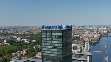 Orbiting-around-top-of-tall-modern-building-with-advertisement.-Aerial-view-of-urban-neighbourhood.-Berlin,-Germany